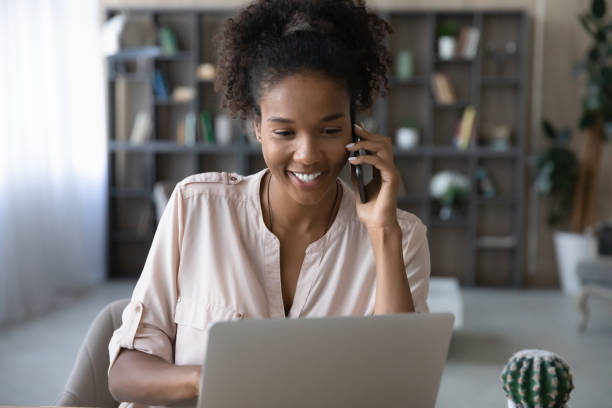 istock Smiling ethnic woman work on laptop talk on smartphone call 1335240326
