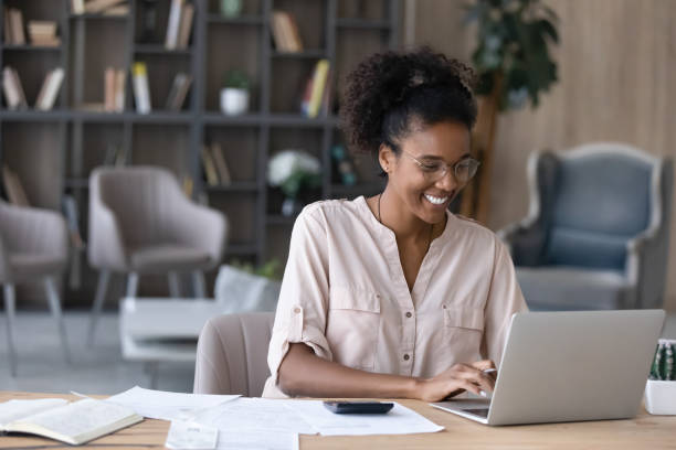 mujer afroamericana sonriente administra las finanzas en una computadora portátil - posición elevada fotografías e imágenes de stock