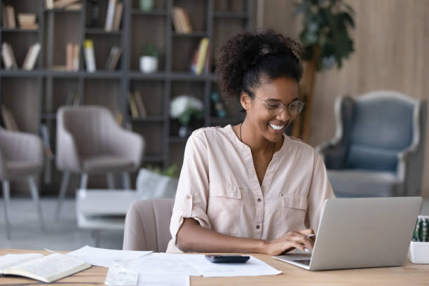 sorridente donna afroamericana gestisce le finanze su laptop - 1 serving foto e immagini stock