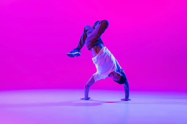 istock Young stylish man, break dancing dancer practicing solo in modern clothes isolated over bright magenta background at dance hall in neon light. 1335243808