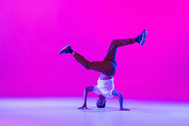 istock Young stylish man, break dancing dancer practicing solo in modern clothes isolated over bright magenta background at dance hall in neon light. 1335243822