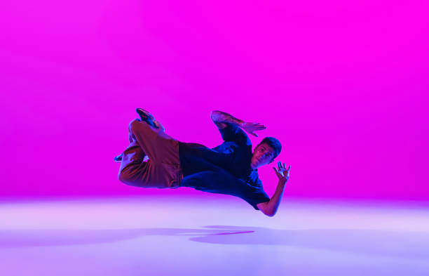 istock Young stylish man, break dancing dancer practicing solo in modern clothes isolated over bright magenta background at dance hall in neon light. 1335243824