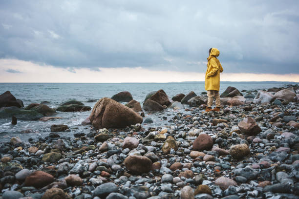 femme portant un imperméable jaune marchant sur la plage un jour de pluie - beach nature outdoors overcast photos et images de collection