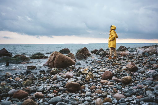 Woman wearing yellow raincoat walking on the beach on a rainy day