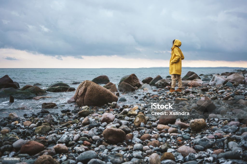 Woman wearing yellow raincoat walking on the beach on a rainy day Raincoat Stock Photo