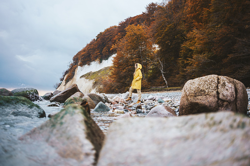 Woman wearing yellow raincoat walking on the beach on a rainy day