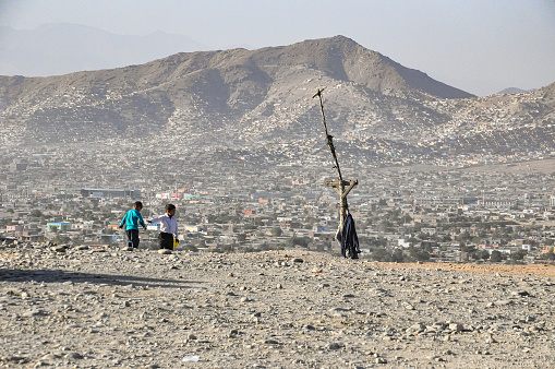 Kabul, Afghanistan Aug 2012: Two kids playing on the sandy hills over Kabul city