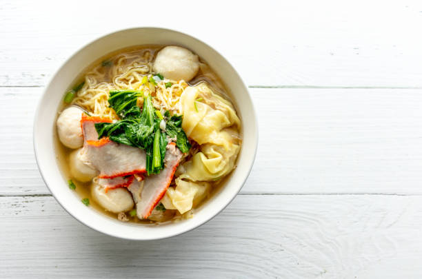 vista superior de wonton y sopa de fideos de estilo chino, col china (bok choy) y carne de cerdo roja sobre fondo de madera blanca. comida callejera tailandesa - noodle soup fotografías e imágenes de stock