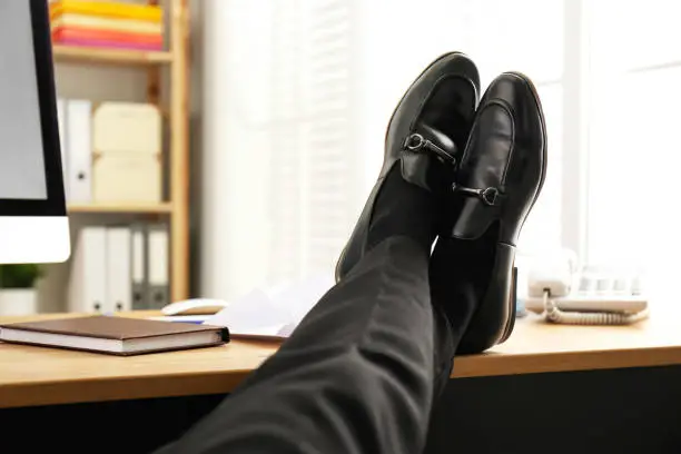 Photo of Lazy employee resting at table in office, closeup of legs