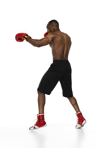 Sporty man during boxing exercises. Photo of boxer on isolated on white background. Strength, attack and motion concept. Fit african american model in movement. Afro muscular athlete in sport uniform