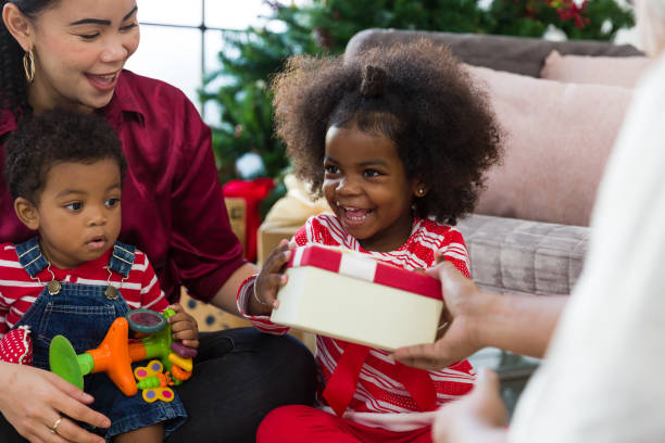 happy african american family enjoying christmas holiday. cute african american little smiling girl receiving christmas gift box or presents gift from adult hand. merry christmas and happy holidays - family american culture african culture black imagens e fotografias de stock