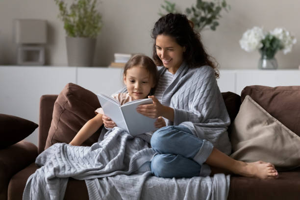 istock Happy mom and daughter kid wrapped in plaid reading book 1335262734