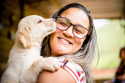 Smiling woman hugging her cute little labrador retriever puppy in her arms while standing outside in the summer