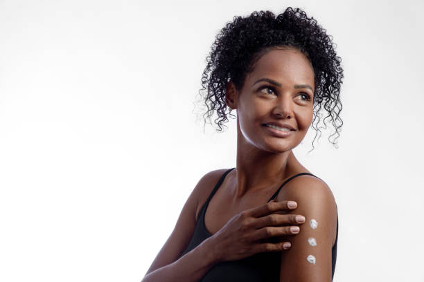 istock Young woman applying moisturizer to her body in studio with light gray background. 1335278336