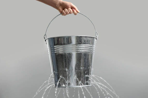 mujer sosteniendo un cubo con fugas con agua sobre fondo gris claro, primer plano - cubo fotografías e imágenes de stock