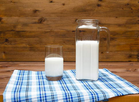 A jug and glass of milk on wooden table, on wooden background.