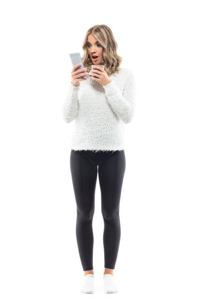 istock Online shopping from home. Young amazed woman with coffee using smart phone checking prices 1335288992