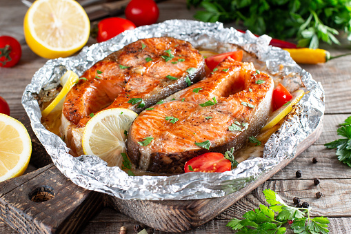 Grilled salmon fish with seasoning and various vegetables on wooden table