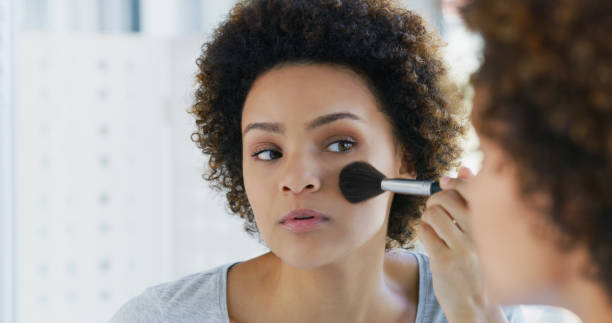 istock Shot of a young woman using a makeup brush on her face while looking into the mirror 1335291442