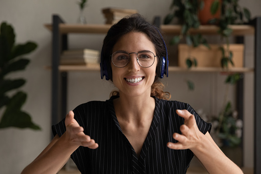 Head shot portrait of smiling woman in headphones speaking at camera, leading internet meeting or lesson, teacher coach shooting webinar, friendly businesswoman consulting client online, video call