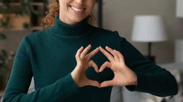 Cropped close up smiling grateful woman showing heart sign, gesture, expressing love and care, happy thankful young female volunteer supporting sick people, regular medical checkup promotion
