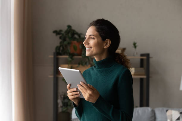istock Smiling dreamy woman distracted from tablet, looking out window 1335296834