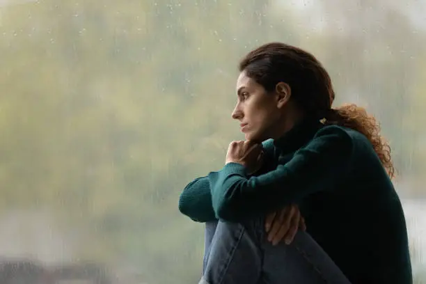 Side view frustrated thoughtful woman looking out rainy window in distance alone, lost in thoughts, upset unhappy young female feeling lonely and depressed, thinking about relationship problems