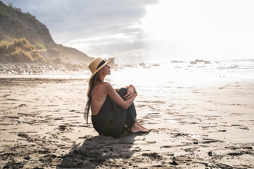 Mujer tranquila sentada sola en la playa durante la puesta del sol, respirando, meditando. photo
