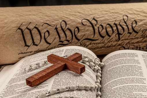 A holy bible and crucifix rest atop a podium with the United States Constitution in the background, which is emblematic of freedom of religion without persecution.