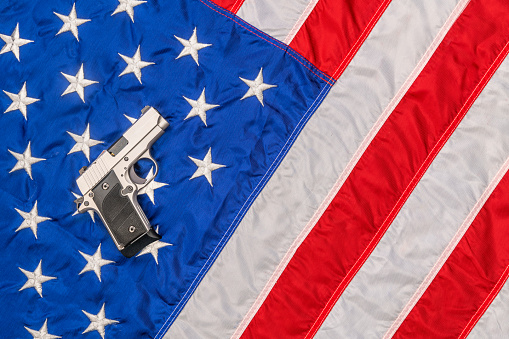 A chrome pistol rests atop an American flag symbolizing freedom and the Second Amendment's right to bear arms.