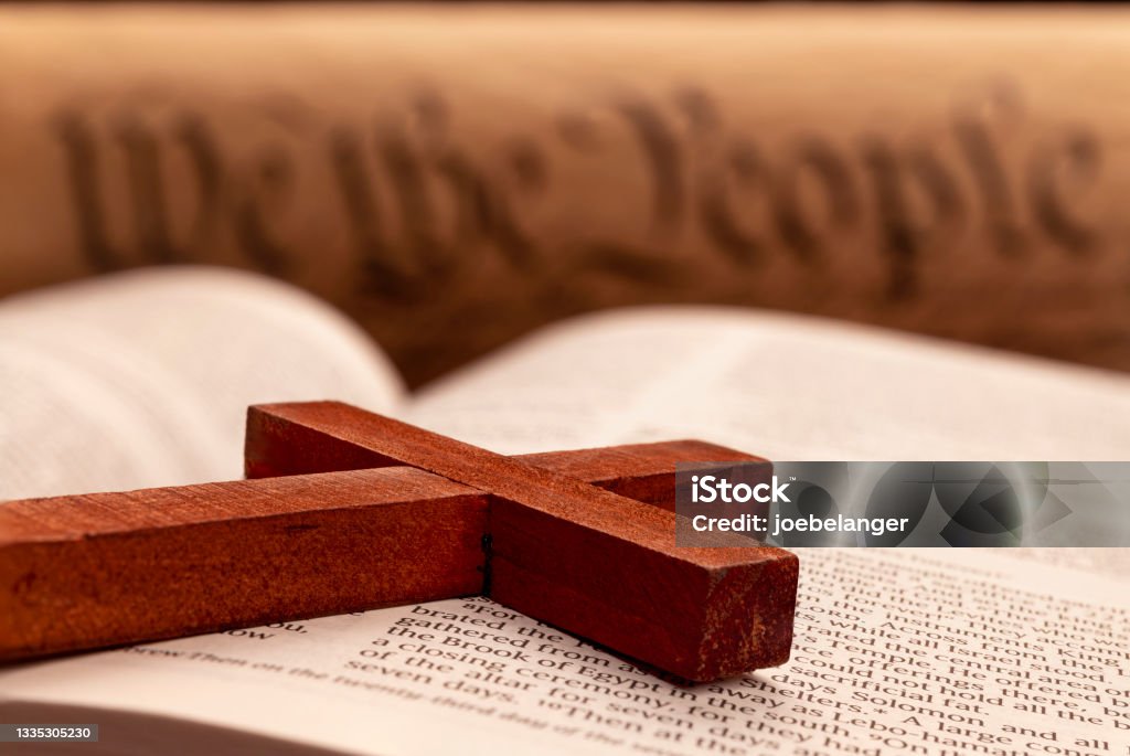 Crucifix on Bible Close up of a religious cross atop the pages of a bible with the constitution in the background. Religion Stock Photo