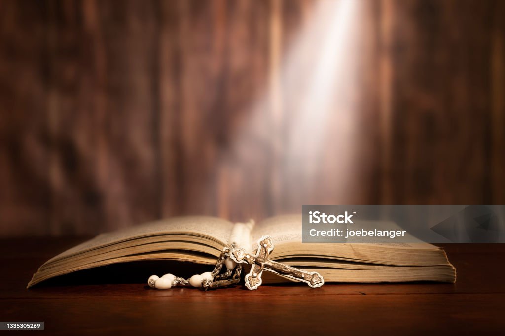 Rosery across a bible Dramatic image showing a bright light beam shining on an old bible with a rosary laying in front of it. Bible Stock Photo