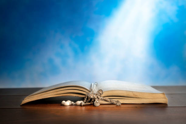 Dramatic image showing a bright light beam shining on an old bible with a rosary laying in front of it.