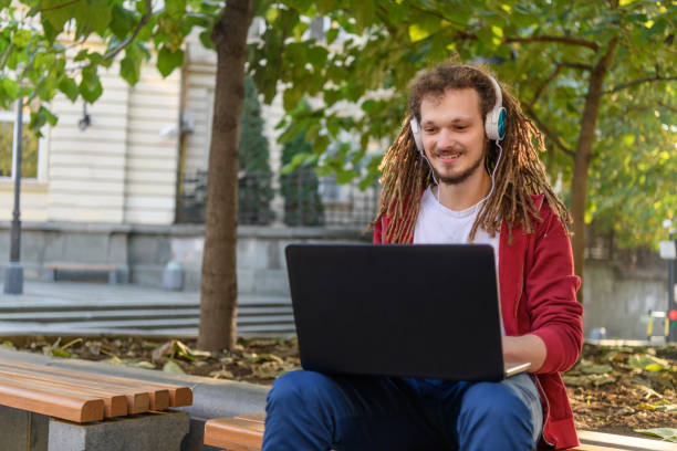 istock Handsome Young Man is Working on a Laptop in Public Park while Sitting on a Bench. 1335306051