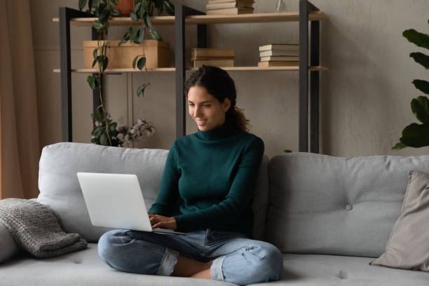 istock Smiling young woman relaxing on couch with laptop on laps 1335308871