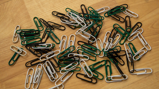 Top view of full paper clips scattered on wooden background. It is device used to hold sheets of paper together made of steel wire bent to a looped shape. Selective focus.