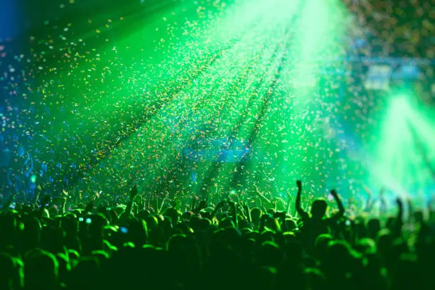 Photo of A crowded concert hall with scene stage green lights, rock show performance, with people silhouette