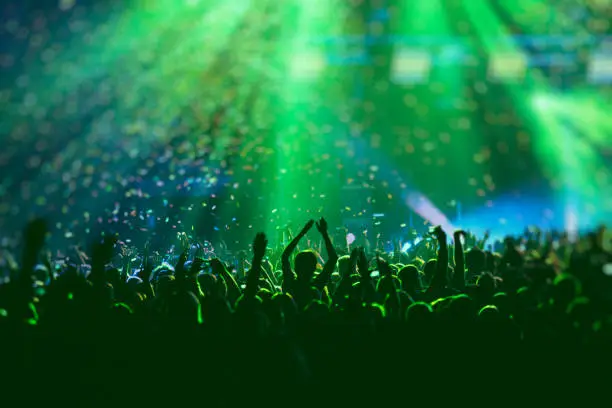 Photo of A crowded concert hall with scene stage green lights, rock show performance, with people silhouette