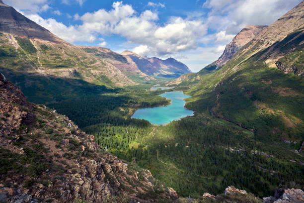 A Look down The Valley from Swiftcurrent Pass in Glacier National Park, Montana - Cropped View The play of light on the valley floor as the clouds shifted provided a constantly changing ethereal scene as the waters of Bullhead Lake below Swiftcurrent Pass show off their glacial tinge moody sky stock pictures, royalty-free photos & images