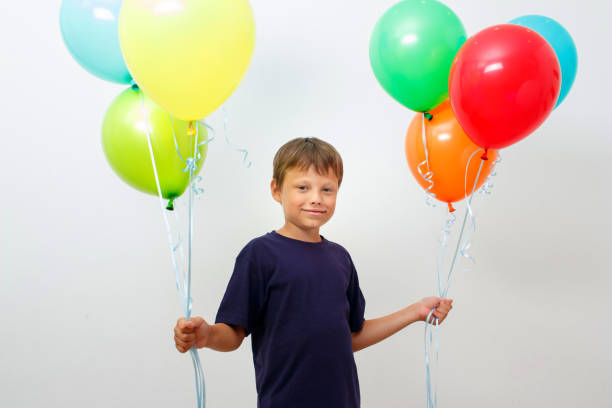 glücklicher achtjähriger junge mit einem arm voller bunter luftballons feiert geburtstag. - 9 year old stock-fotos und bilder