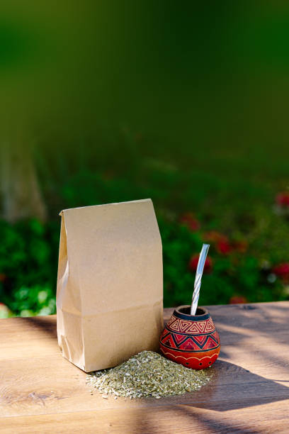 その上に散らばったイェルバの仲間と木製のテーブルの上にカラバッシュで作られた伝統的な仲間と茶色の紙の素朴なパック。 - yerba mate package hot drink food ストックフォトと画像