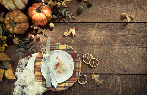 Autumn place setting and a centerpiece candle with pumpkins, gourds and holiday decor arranged against an old wood background