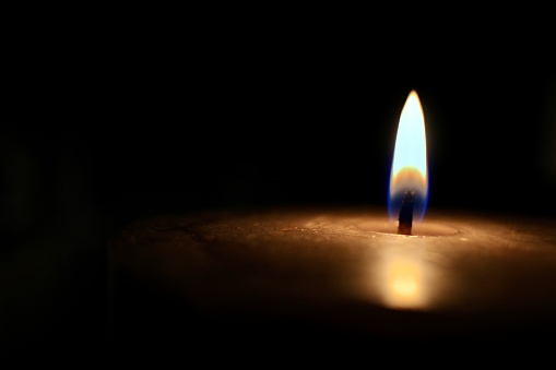 Closeup isolated candle glowing in pitch darkness.