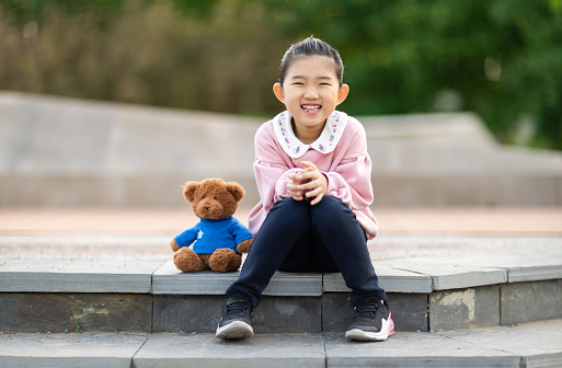 Happy indian girl kid hugging her big teddy bear isolated over beige studio background.