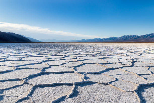 Sunrise over Badwater Basin, Death Valley, California. Sunburst over mountains in the distance; foreground covered with white salt formations with hexagonal shapes. Sunrise over Badwater Basin, Death Valley, California. Sunburst over the far mountains; the basin floor is covered with white salt deposits; snaking crystal formations form hexagonal shapes into the distance. death valley national park stock pictures, royalty-free photos & images