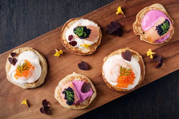 Blinis made with; flour, buckwheat flour, egg yolks, yeast, milk and egg whites. You can create your own recipe, here shown with; beetroot infused creme fraiche, smoked salmon, caviar of course, topped with dill. Colour, horizontal format with some copy space.