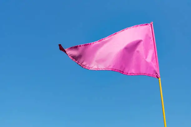 Photo of Pink flag waving in the wind against clear blue sky