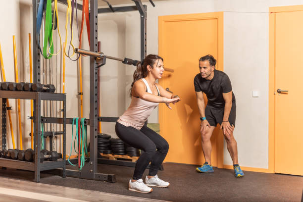 istock Young woman doing squats without weighting exercise with trainer in gym 1335362326