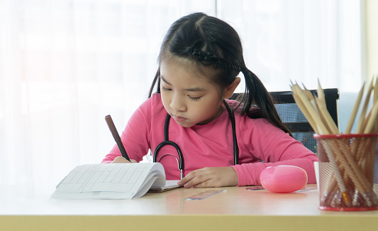 Asian children girls learning doing homework drawing at home. Portrait of cute daughter elementary school education Reading books and take notes development.