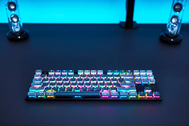 istock Color backlighted gaming computer keyboard laying on grey desk. Blue illuminated wall. 1335367973